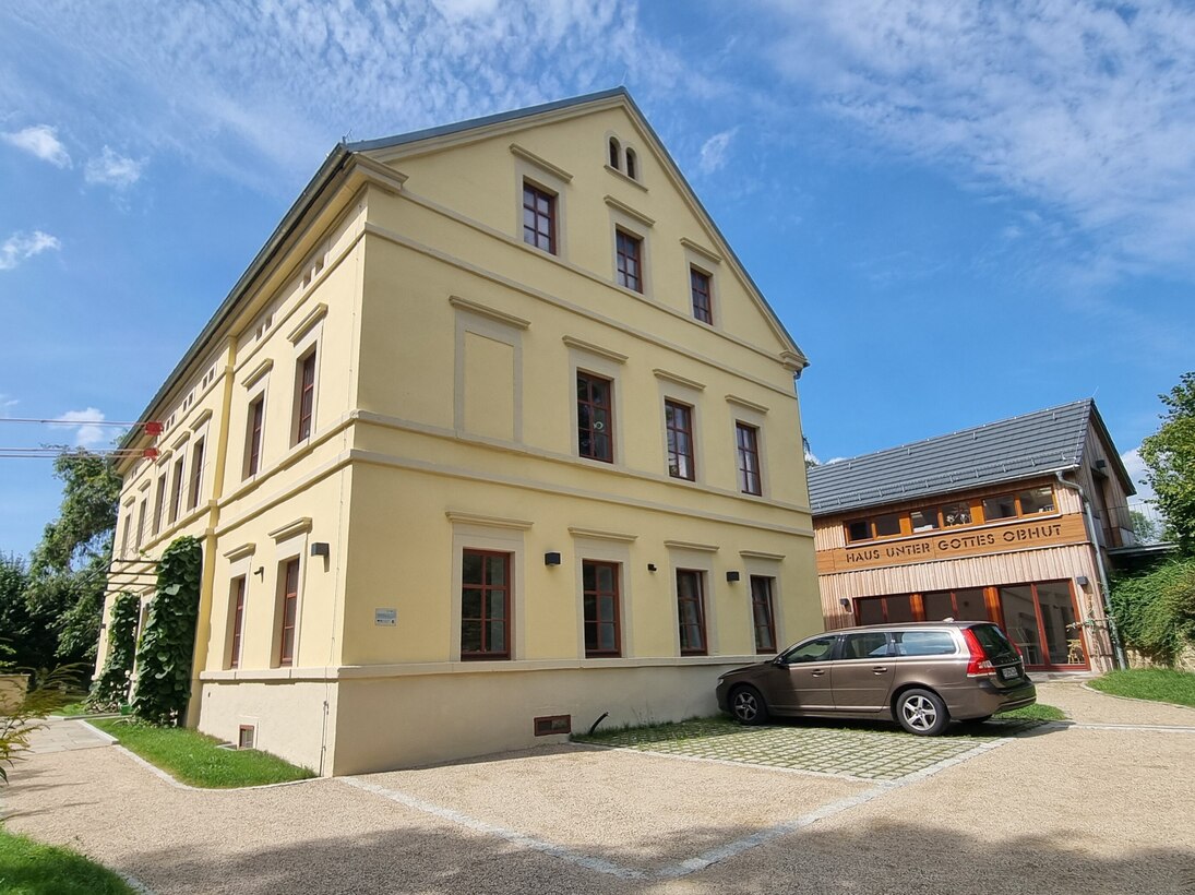 beigefarbenes Haus mit drei Parkflächen nebst holzverkleideter neuer Scheune im Hintergrund