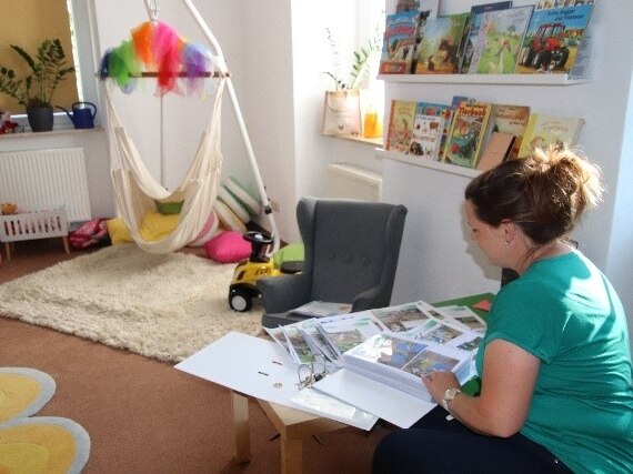 Spielzimmer mit Hängesitzmatte, kleinem Kindersessel, Spielzeug und einer Regalwand mit Büchern